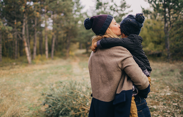 mother holding her kid and kissing their head in the woods