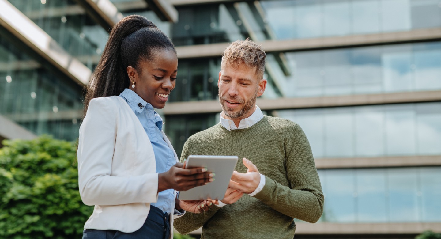 Two coworkers talking about something on a tablet while outside the building