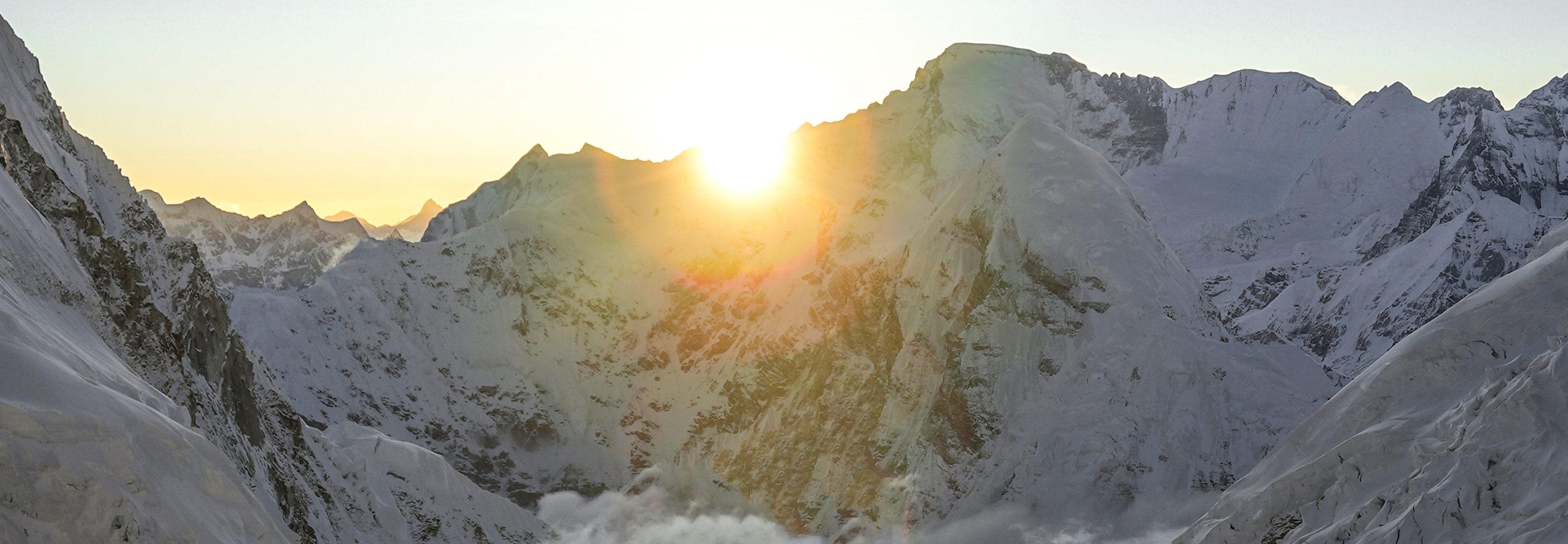 Sun peaking through snowy mountain peaks