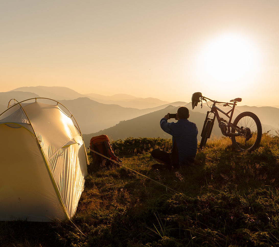 person next to their tent and bike on a hill