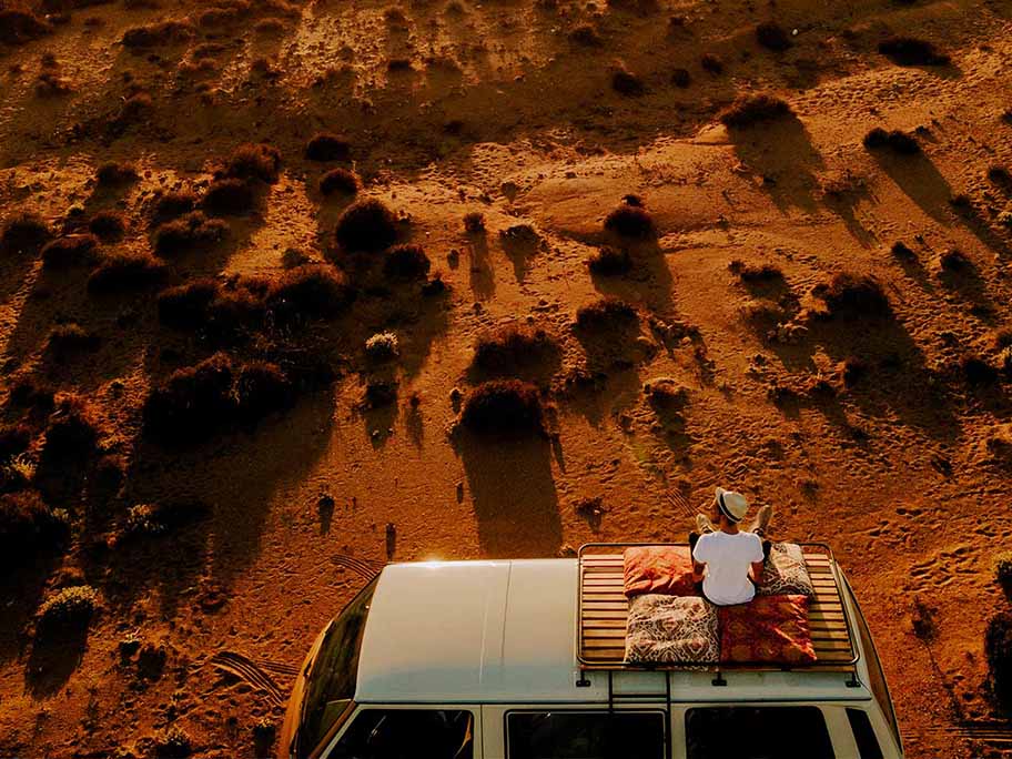 person sitting on top of their van in a red sand environment
