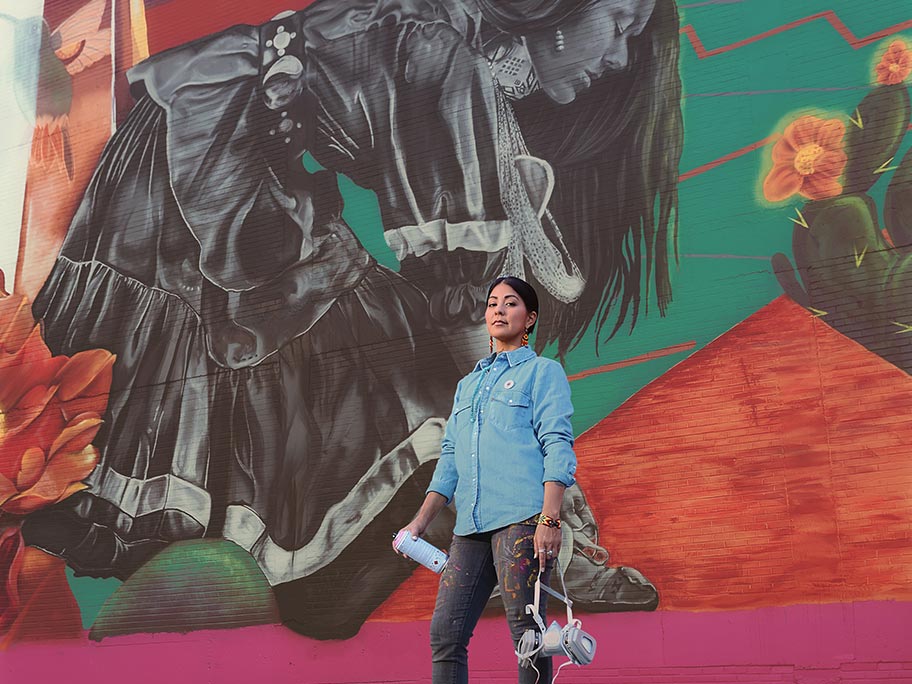 Artist LaMorena posing in front of a mural