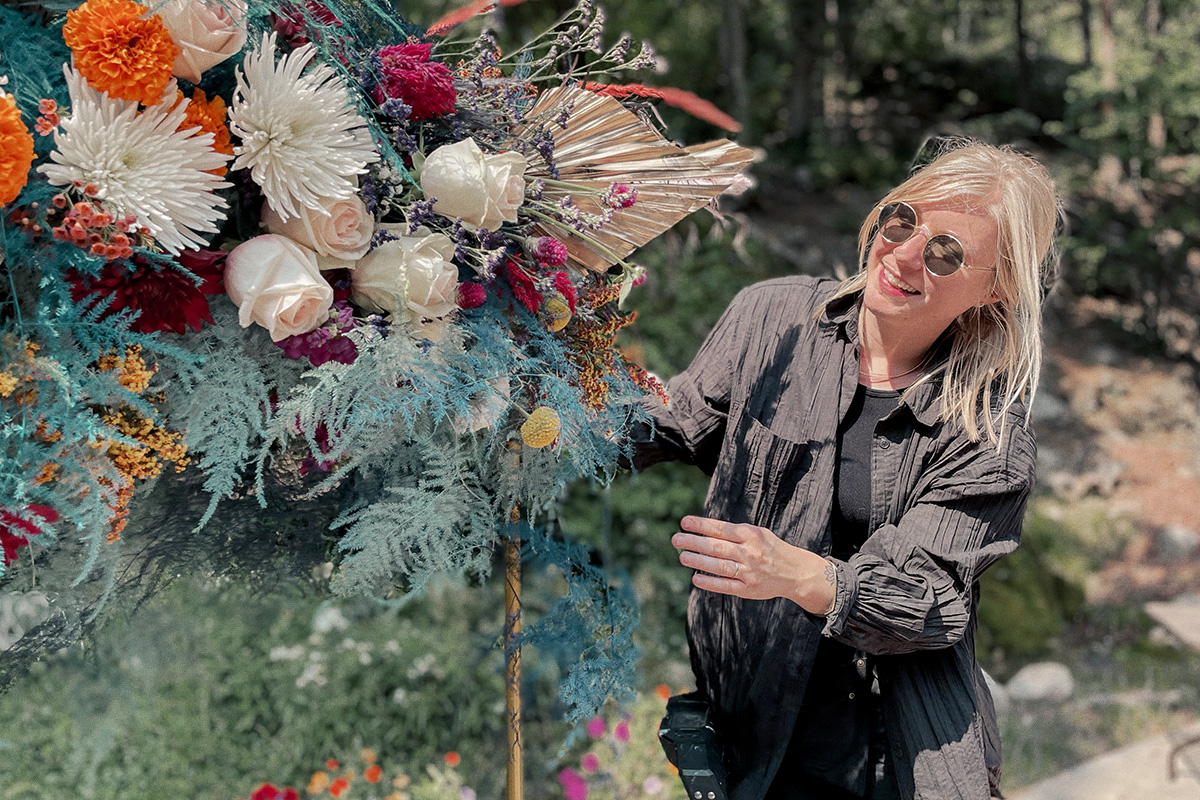 woman in sunglasses adjusts large floral arrangement at outdoor wedding
