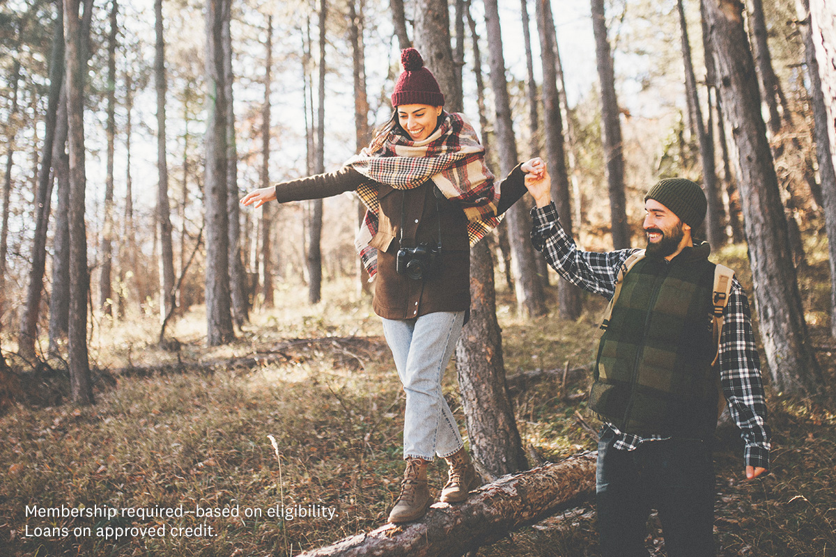 woman balancing on fallen log holding man's hand