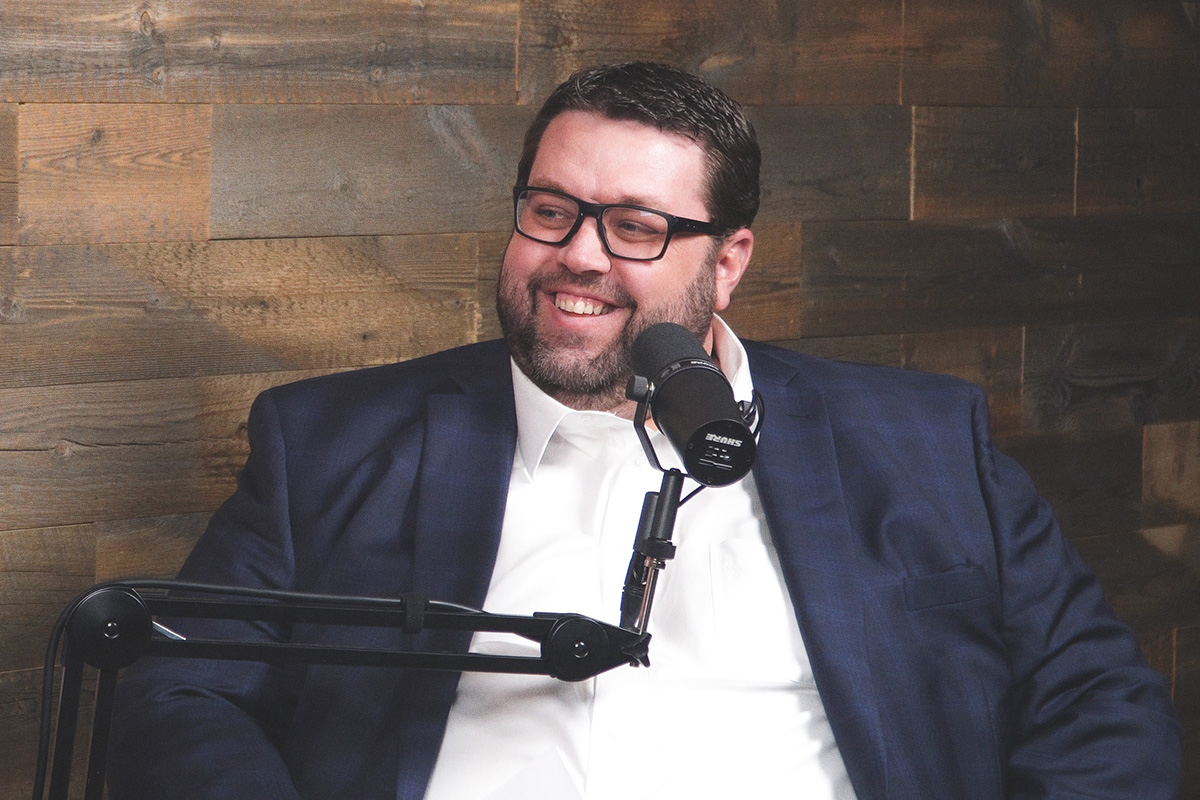 bearded man in white shirt and glasses at the podcast mic