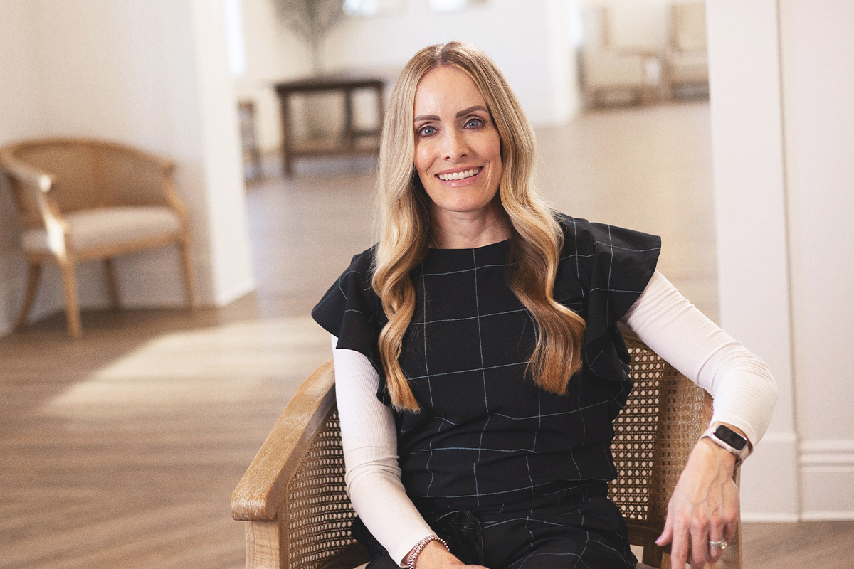 woman with long blonde hair and black and white top sitting in chair in event center
