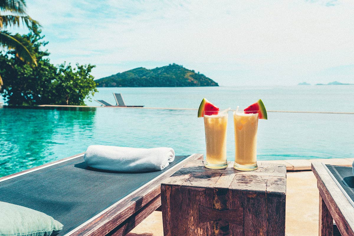 two yellow drinks next to a lounge overlooking the ocean