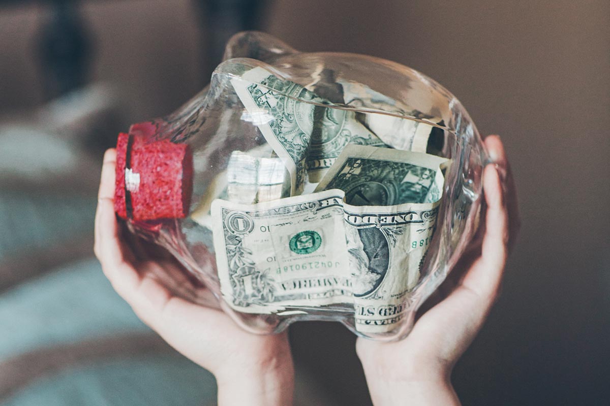 kid holding a glass piggy bank with cash in it