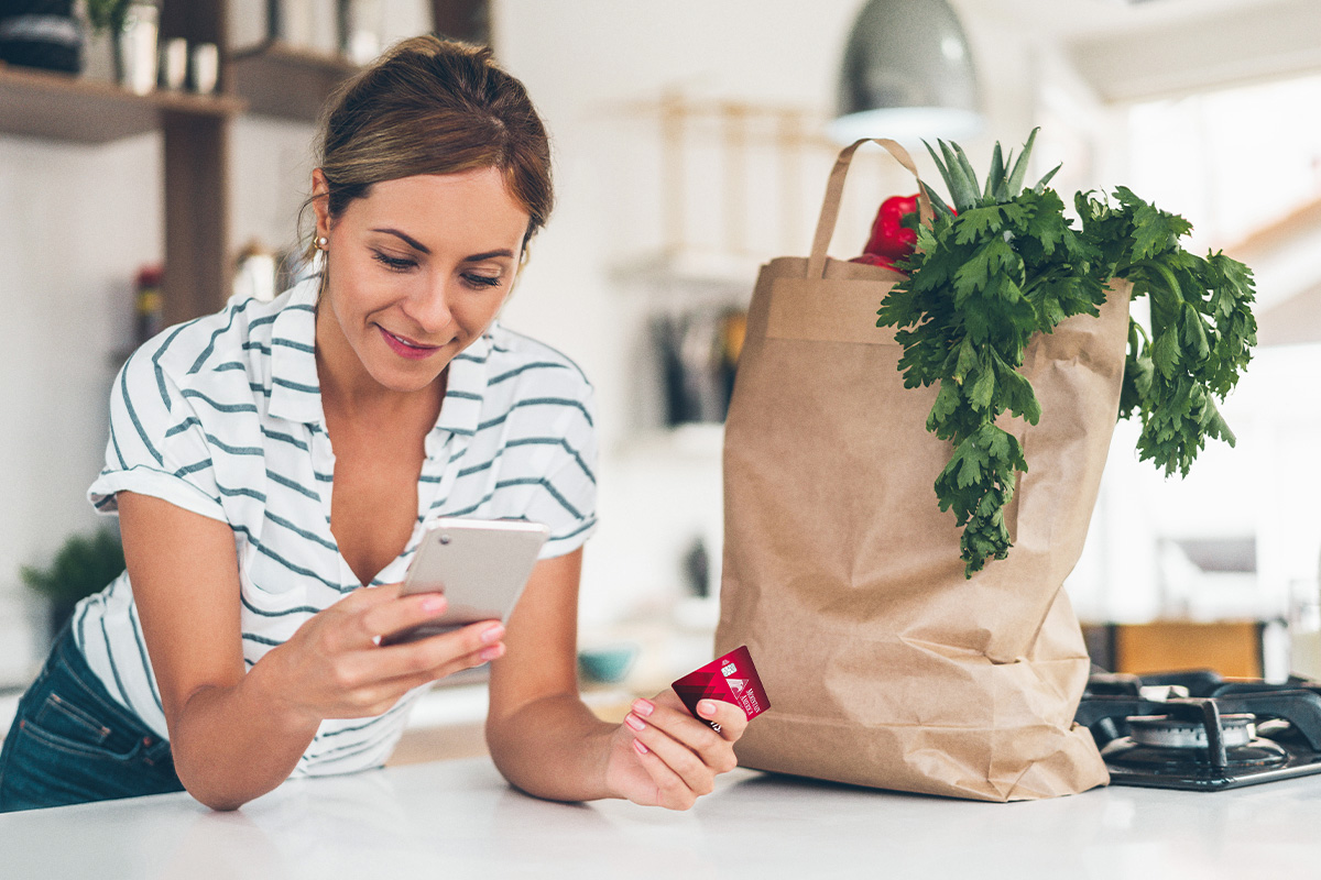 woman leaning on her kitchen counter while holding her Mountain America card