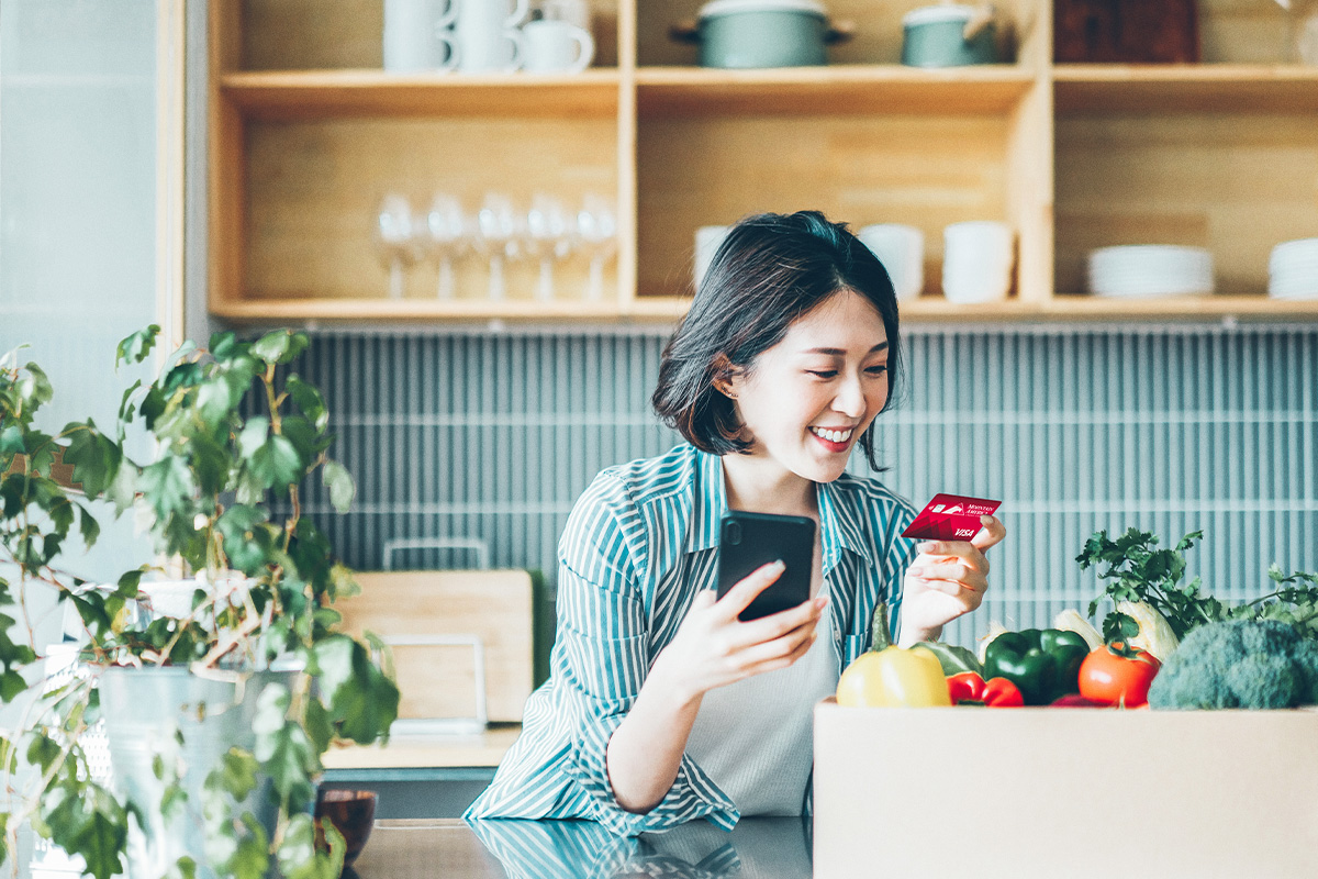 woman in kitchen purchasing something on mobile phone with credit card
