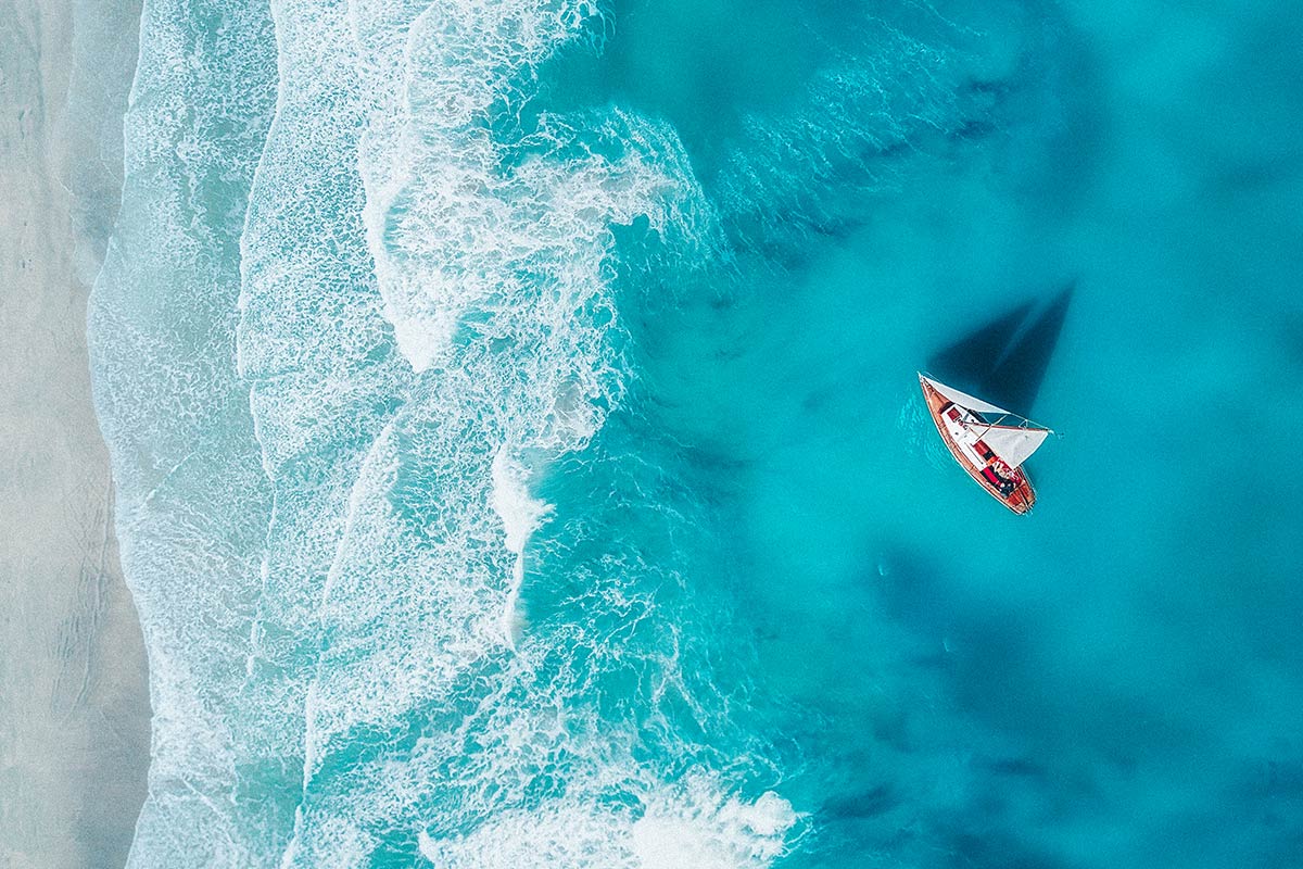 aerial view of an ocean shoreline with a sailboat in the water
