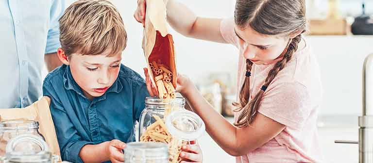 Two kids pouring dried pasta into jar